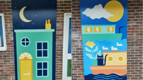 St Barnabas Primary School Murals on the side of the school building depicting a cat on a boat and ducks in the water, and a Jericho house at night.