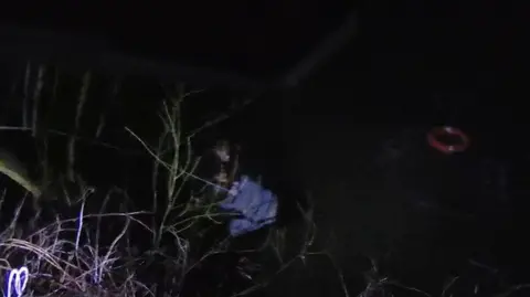 Durham Police Two teenagers cling to a branch in the River Wear. An orange buoy floats in the river behind them having just been thrown in by police officers.
