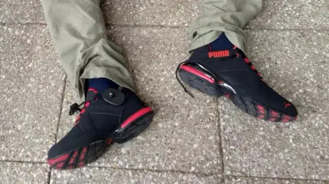 A view of the shoes worn by a man sat on a paved floor, both a right