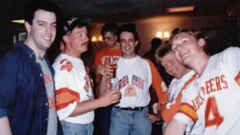 Bucs UK Gareth and a group of other Bucs fan at a meeting. All are looking at the camera and smiling. They are wearing Bucs merchandise, which was orange and white. 