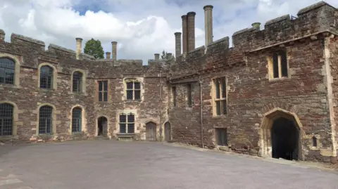 Google A screenshot from Google showing the inside courtyard of Berkeley Castle. It is an old brick castle with crenellated ramparts, chimneys, arched doorways and leaded cross windows.