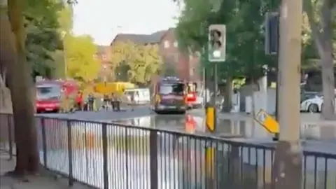 A road flooded with water, with two fire engines seen parked on the road.
