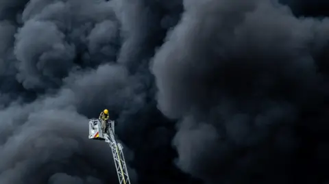 Pacemaker A fire fighter on a ladder stands in front of a blanket of thick black smoke