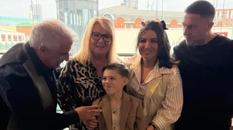 Marisa Billitteri Lucciano with his family. From left to right, his grandfather, his grandmother, his mother and then father. They are standing around him smiling.