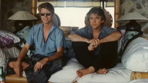 George Underwood David Bowie and George Underwood sitting on a sofa in Mustique