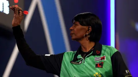 PA Media Deta Hedman, wearing a green and black shirt, takes aim with a dart. She looks focused at the oche.