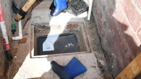 Greater Manchester Police A hole in the pavement floor of a shed where a grey safe has been uncovered 