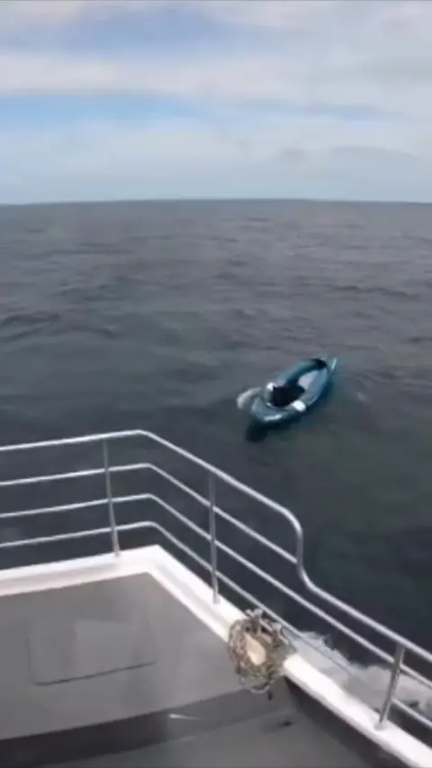 A black dog is sitting in a blue kayak a few metres away from the front of the boat.