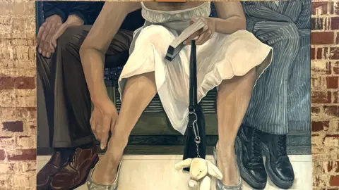 Contributed A painting of a woman sat on a tube who has spread her legs wide. She is encroaching on two men wearing suits sat beside her who have angled their legs away from her. The woman is wearing a white summer dress and has a black bag with a rabbit key chain attached to it that rests on the floor between her legs. She holds a book in one hand and her other hand is down toward her ankle.