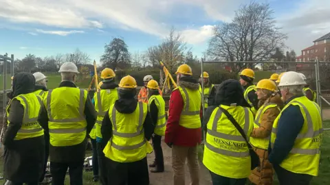A group of about 10 people in hi vis jackets and hard hats within the precinct of the castle