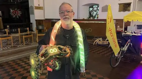 Andy Payne from Mechanismo Ltd holds a Crawlybot and has a Lightsnake around his neck in the knave of St George's Church, Gravesend