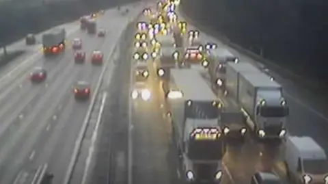 Travel builds up on the M6 with cars and lorries, with their lights on, come to a halt in the dark with traffic flowing on the other carriageway