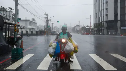 A motorcyclist with weights added to his motorbike on a road in Taiwan, caught in powerful winds and heavy rain.