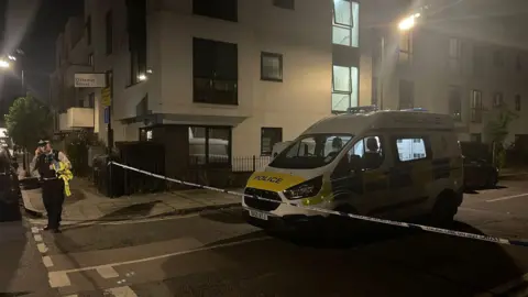 A police cordon and police van and police officer on the phone