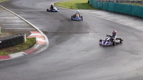 Shaun Whitmore/BBC Three karts and drivers can be seen entering a corner at a race circuit.