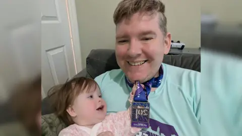 Scott Storey Scott Storey with his baby daughter, who's playing with a medal hanging from a ribbon around his neck.