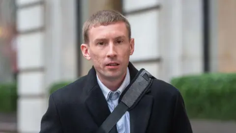 Chris Head, pictured outside wearing a black coat with a black bag strap across his body