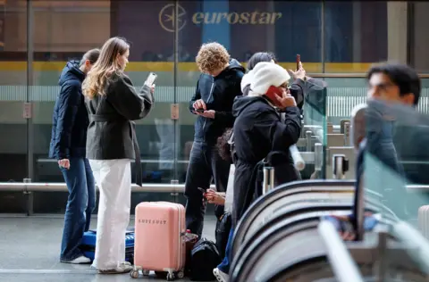 Tolga Akmen / EPA People wait at the top of escalators with luggage and checking phones at the Eurostar terminal at St Pancras in London, in December. The Eurostar sign can be seen in the background.