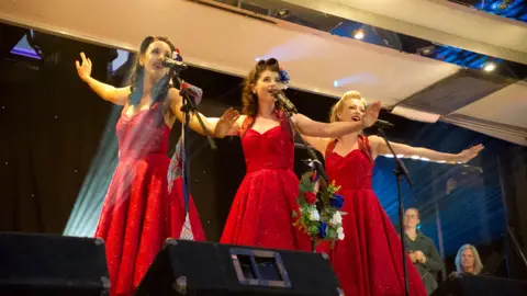 Three female singers in red 1940s dresses