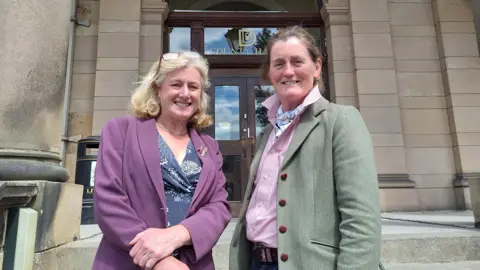 Two women stood outside a grey stoned building 