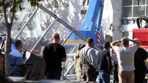 Men stand in front of a crane and a smashed glass structure outside a railway station in Serbia