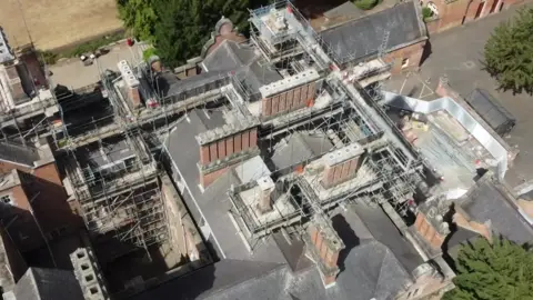 An drone-taken aerial view of scaffolding on top of a large red brick building 