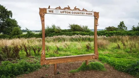 A huge wooden photo frame with cut out rabbits on top frames the lush landscape at a country park