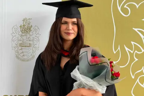 Supplied A woman in graduation clothes clutching a bouquet of red flowers and smiling.