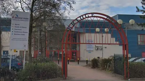 Google Map Exterior view of Bridge Park Community Leisure Centre in showing its entrance archway, fencing, and signage.