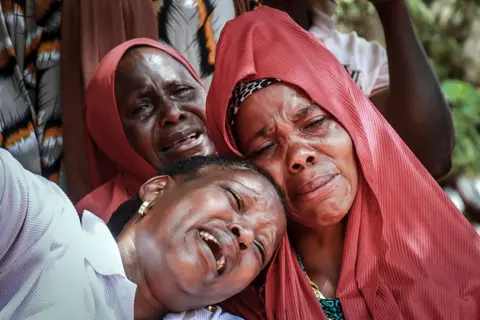 AFP / Getty Images Three female women - two wearing terracotta headscarves - in tears at a funeral in Mwanza, Tanzania - Thursday 6 November 2025. 