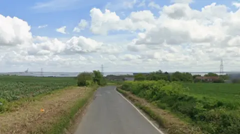 Google two fields lie either side of a road, which is Stoke Road in Hoo St Werburgh. Pylons and housing can be seen on the horizon. The image is a screenshot from Google streetview.