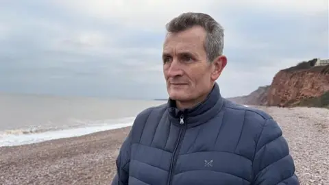 Mike Brown looking to the left and wearing a blue coat.