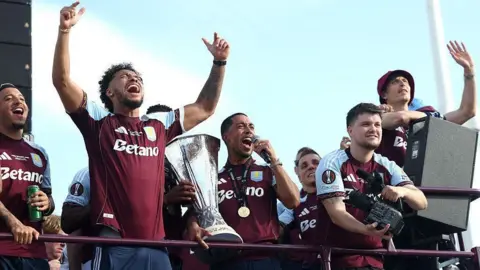 Getty Images Villa players cheer and celebrate on top of a bus.