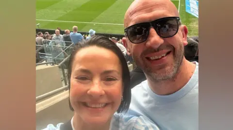 Hayley Finlay Hayley is smiling and standing next to her husband Danny at a Coventry City game. Both are wearing Sky Blues tops. Hayley's dark hair is swept back while Danny is bald and wearing dark glasses and wears designer stubble on his face.