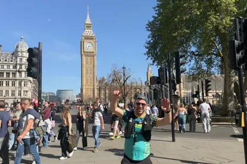 Chris poses in front of Big Ben, his arms in the air.