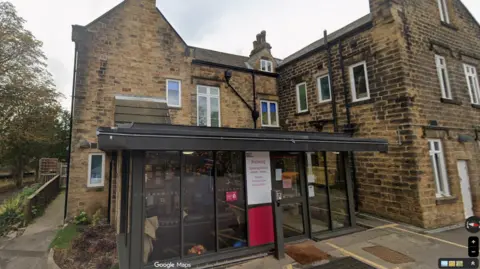 Google A two storey building in stone in a style from the early 1900s.
A single storey wide modern porch has been added to the front with large glass panels in a black frame. In the middle of the porch is a sign which displays the words Sheffield Hallam University Nursery with opening hours listed underneath.