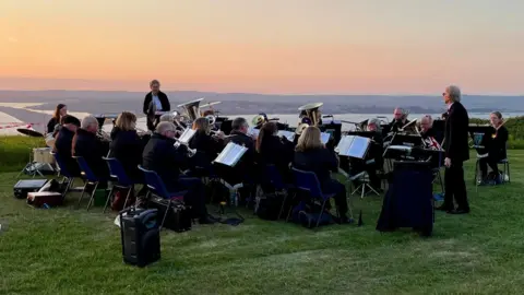 Portland Town Council A brass band playing on top of the hill at Portland overlooking Chesil Beach as the sunset turns the sky orange