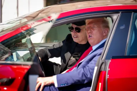 Trump and Musk sitting in a red Tesla with the door open, Trump in the driver's seat