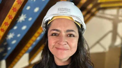 Photo of Ana wearing a white hard hat. She has brown hair. 