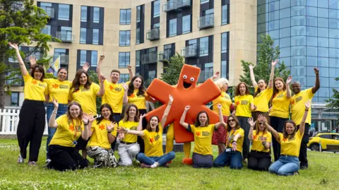 Bristol NHS Foundation Trust A group of people wearing yellow t-shirts, celebrating on a grassy area.