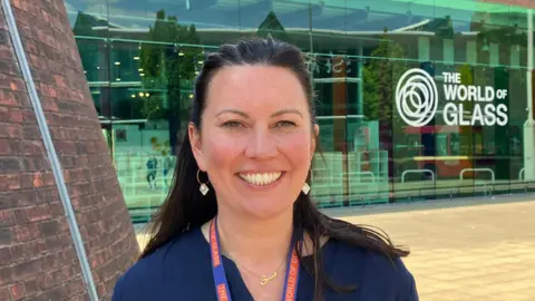 Portrait of Sarah Taylor smiling outside the museum's glass front, which has the World of Glass branding.