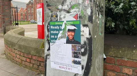 A ripped poster on a electricity box outside Queen's University Belfast. The poster shows a smiling police officer but beneath it is the phrase British policing in Ireland - reject it