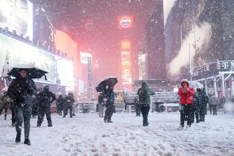 People with umbrellas in a snowy Times Square at night