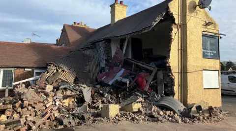 BBC The rear of a two-storey building with yellow walls, with the back wall missing and rubble lying on the ground