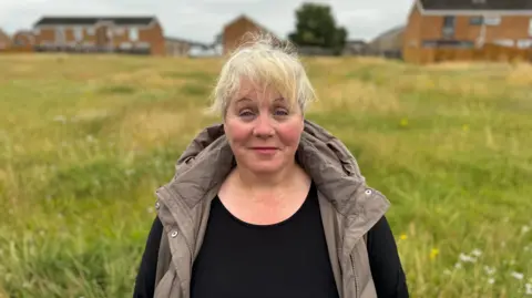 George King/BBC Jane Seaney smiling in a field. She is wearing a black long-sleeved top with a taupe gilet over it