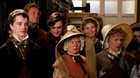 Scene from Cranford featuring a group image of (front row) Alex Etel, Imelda Staunton, Judi Dench, with back row of Tom Hiddleston, Matthew McNulty and Jodie Whittaker