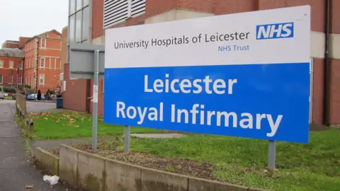 Leicester Royal Infirmary sign with red brick buildings visible in the background