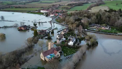 An aerial shot of Severn Stoke at a time of flooding, showing properties partly submerged in water. 