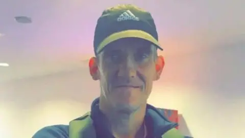 A man aged about 50, wearing a baseball cap. He is staring directly into the camera.