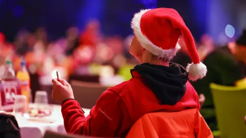 A man wearing a Christmas hat attends an annual Christmas dinner party for needy and homeless people.